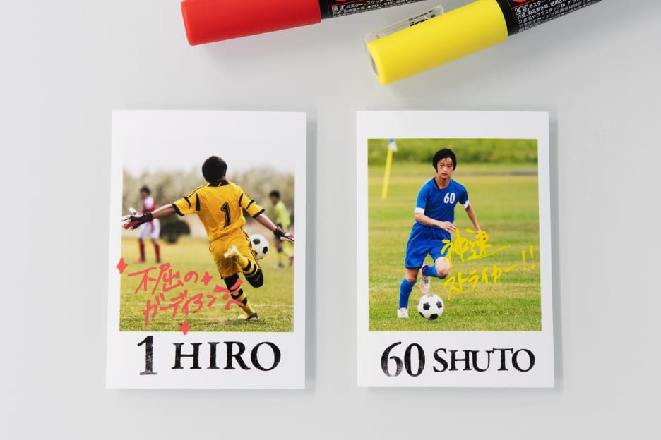 ポスカでキャッチフレーズを書き込んだハーフサイズプリント2枚の写真。「不屈のガーディアン」「神速ストライカー!!」と書いてあります