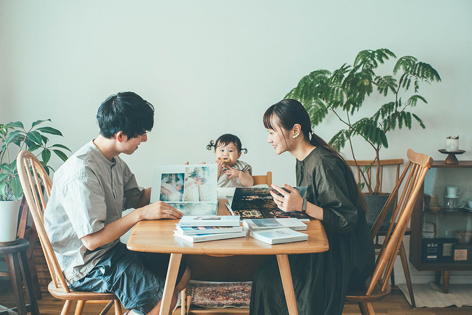 結婚式の写真をプリントした「フォトブック ハードカバー」 を、リビングテーブルで見ている、jyotaさんとmisuzuさんとお子さんの写真