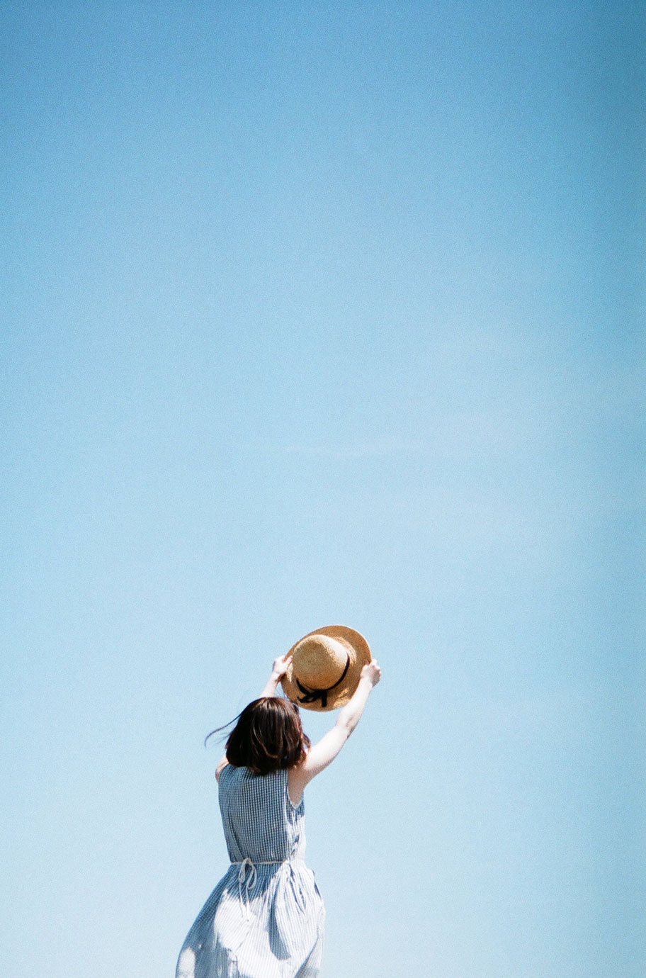 青空に麦わら帽子をかざした女性の写真