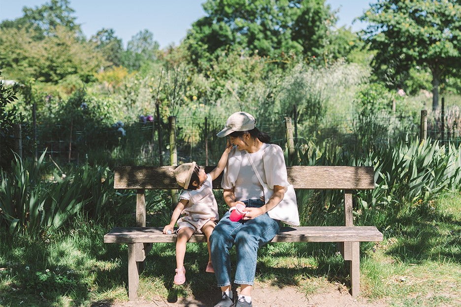 草木を背景に、子どもと女性がベンチに座って向き合っている写真