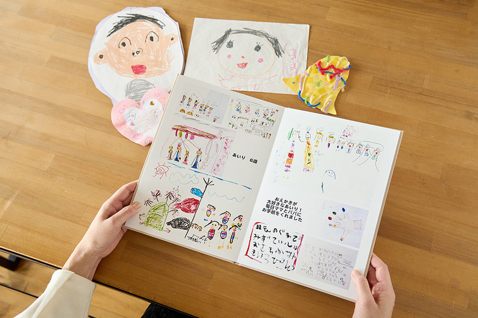 子どもがつくった作品がプリントされたイヤーアルバムを開いている写真