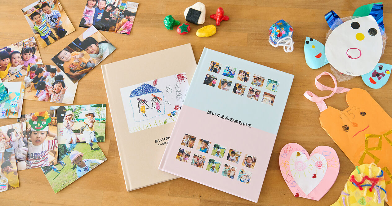 保育園や幼稚園での写真をまとめたイヤーアルバムと、子どものつくった作品をまとめたイヤーアルバムが、写真プリントや工作と一緒に並んだ写真