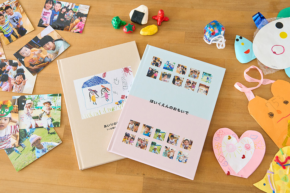 保育園や幼稚園での写真をまとめたイヤーアルバムと、子どものつくった作品をまとめたイヤーアルバムが、写真プリントや工作と一緒に並んだ写真