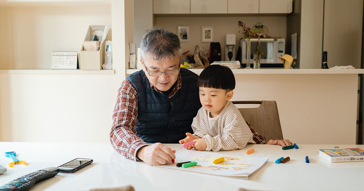 テーブルで祖父と孫が絵を描いている写真