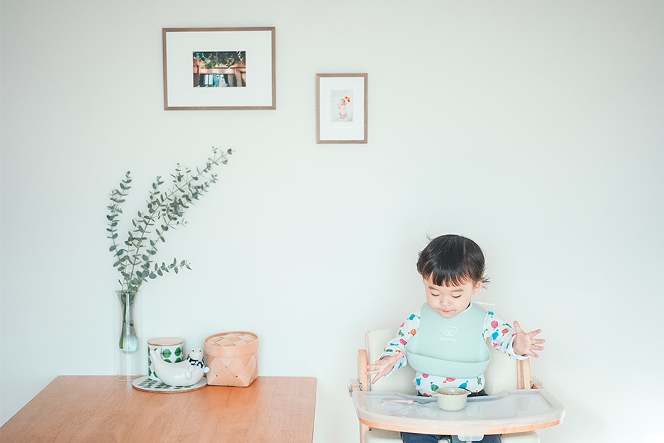 壁に飾られた「frame #001」とベビーチェアに座る子どもの写真