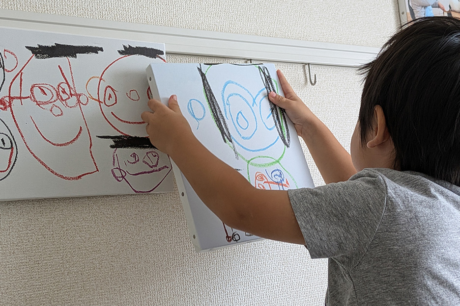 子どもの作品の写真をプリントしたWALL DECORを壁に飾っている子どもの写真